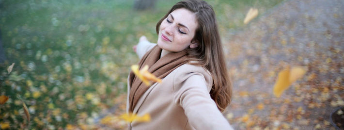 Woman standing outside with arms open, enjoying autumn leaves