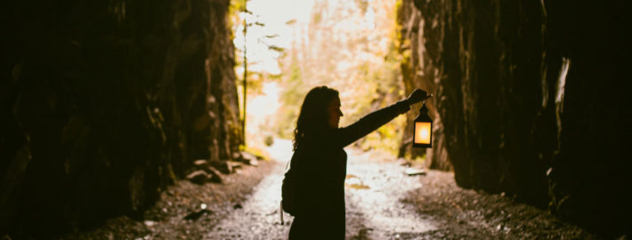 Woman standing in a cave holding a lantern